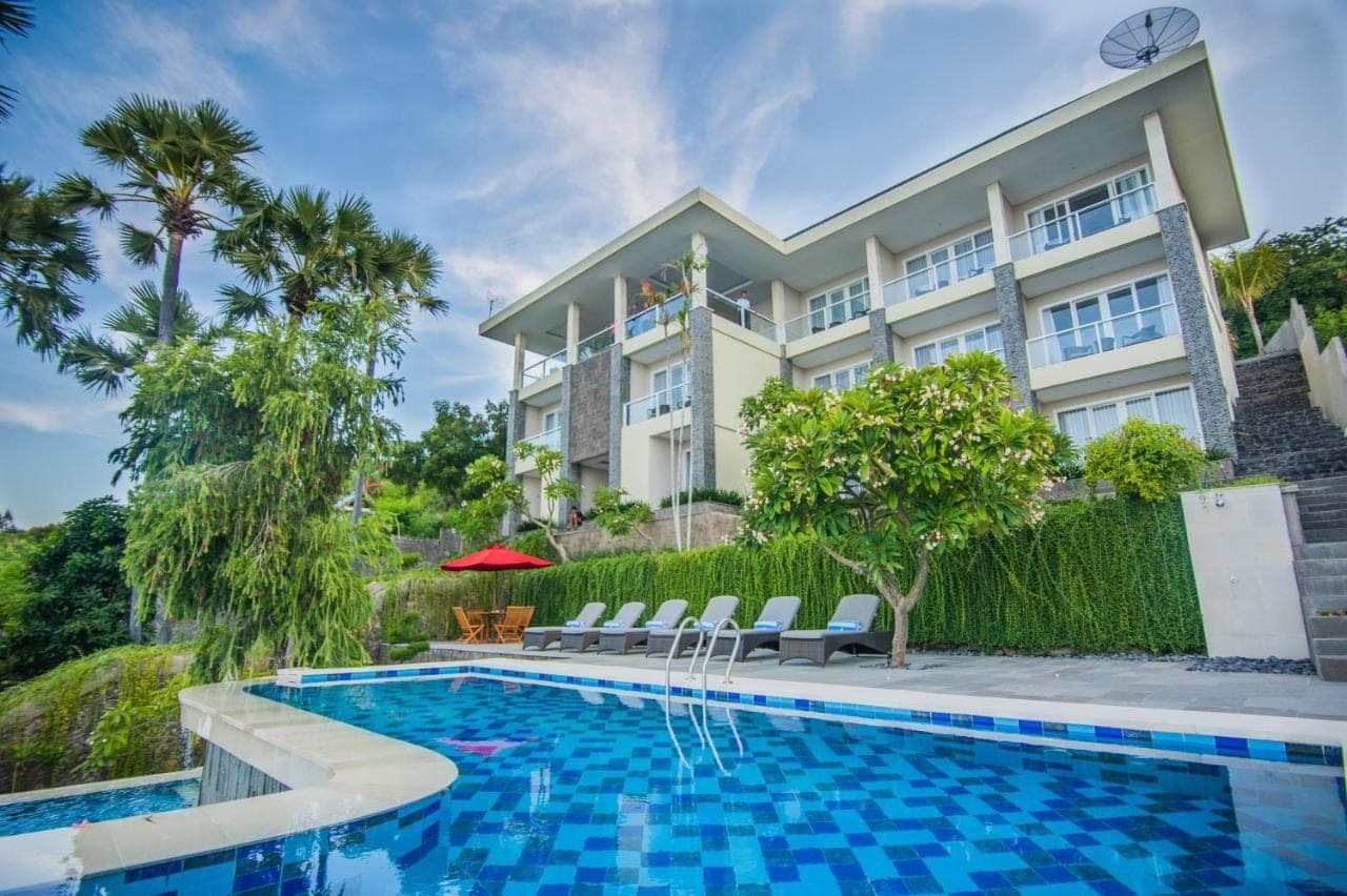 a villa with a swimming pool in front of a building at Ibus Beach Hotel in Amed