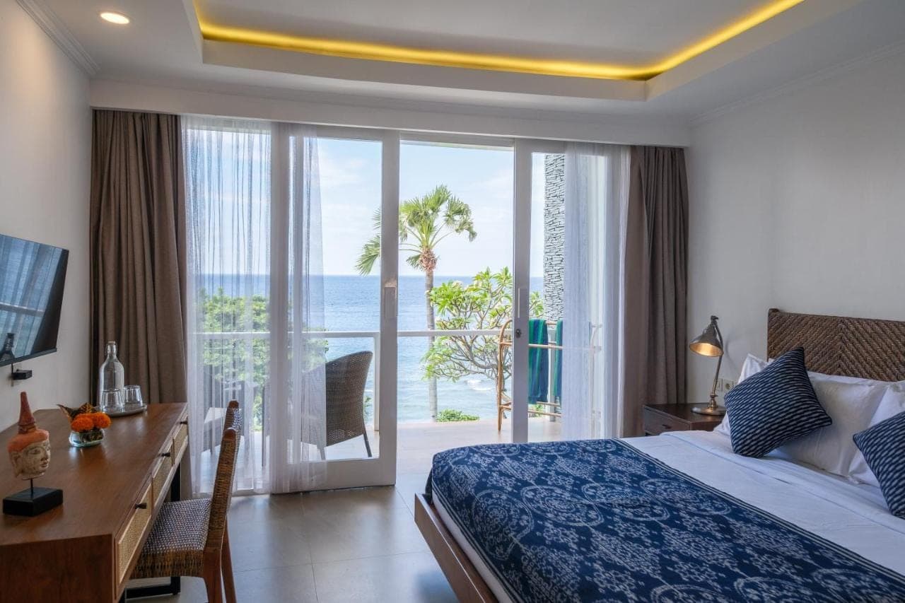 a bedroom with a bed and a desk with a view of the ocean at Ibus Beach Hotel in Amed