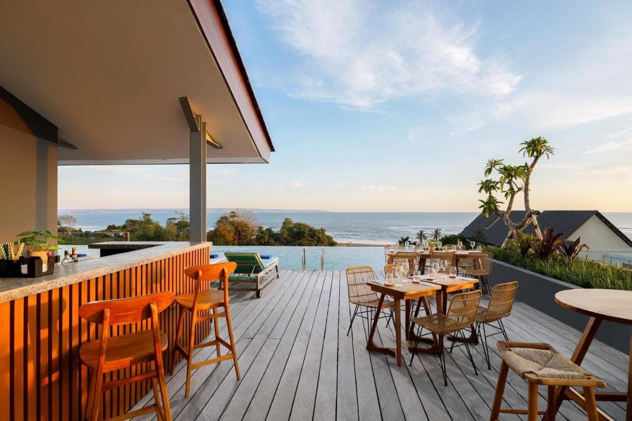 a deck with tables and chairs and a view of the ocean at Citadines Berawa Beach Bali Resort in Canggu