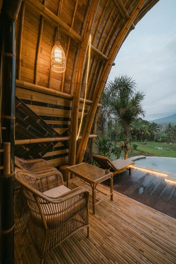 a wooden deck with wicker chairs and a table at Lotus Bamboo House by Arcada Bali in Sidemen