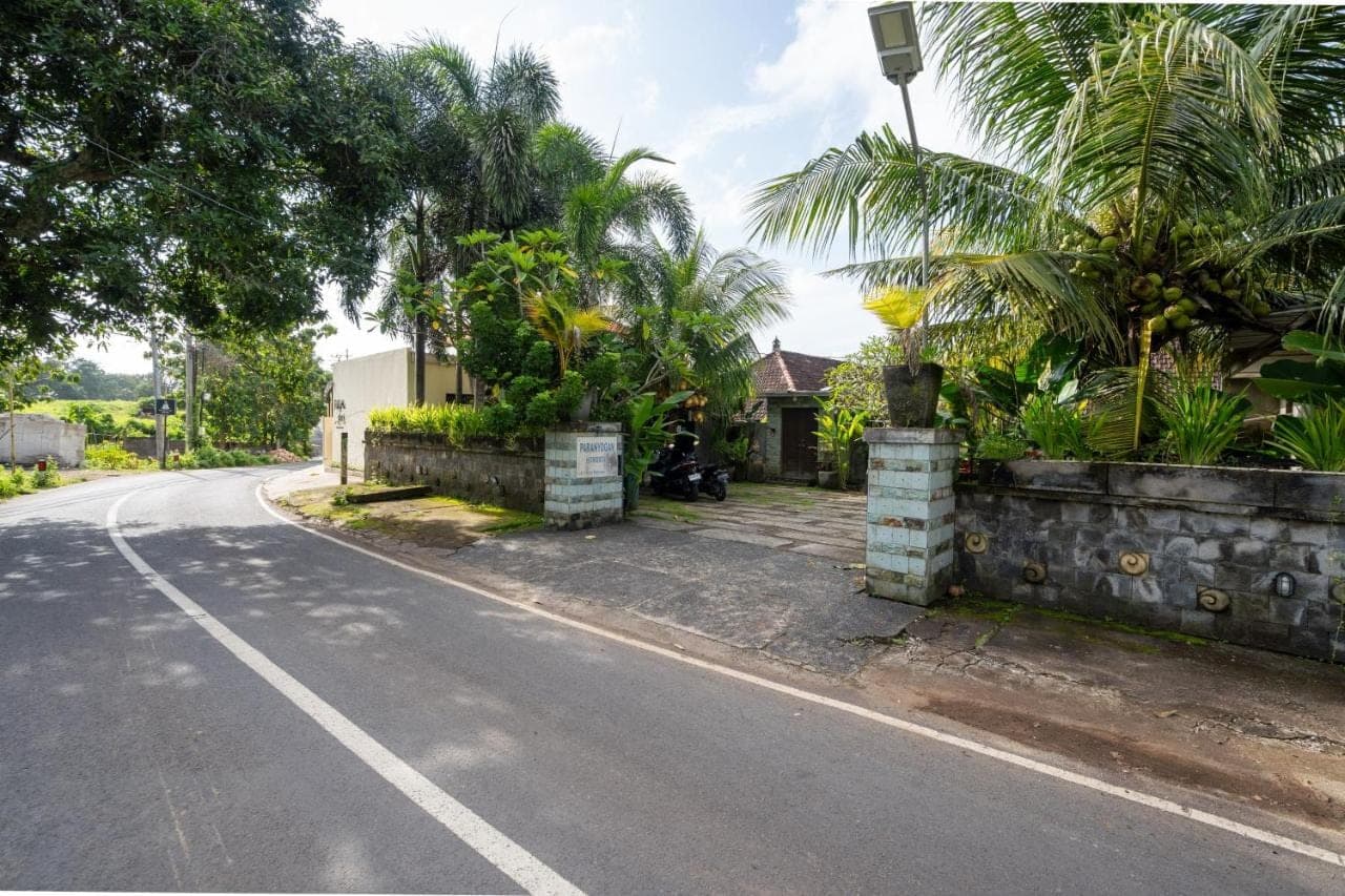 an empty road with a house and palm trees at Paranyogan Homestay in Uluwatu