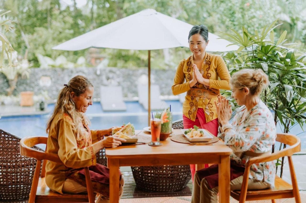 three women sitting at a table with a woman standing at Dewangga Ubud in Ubud