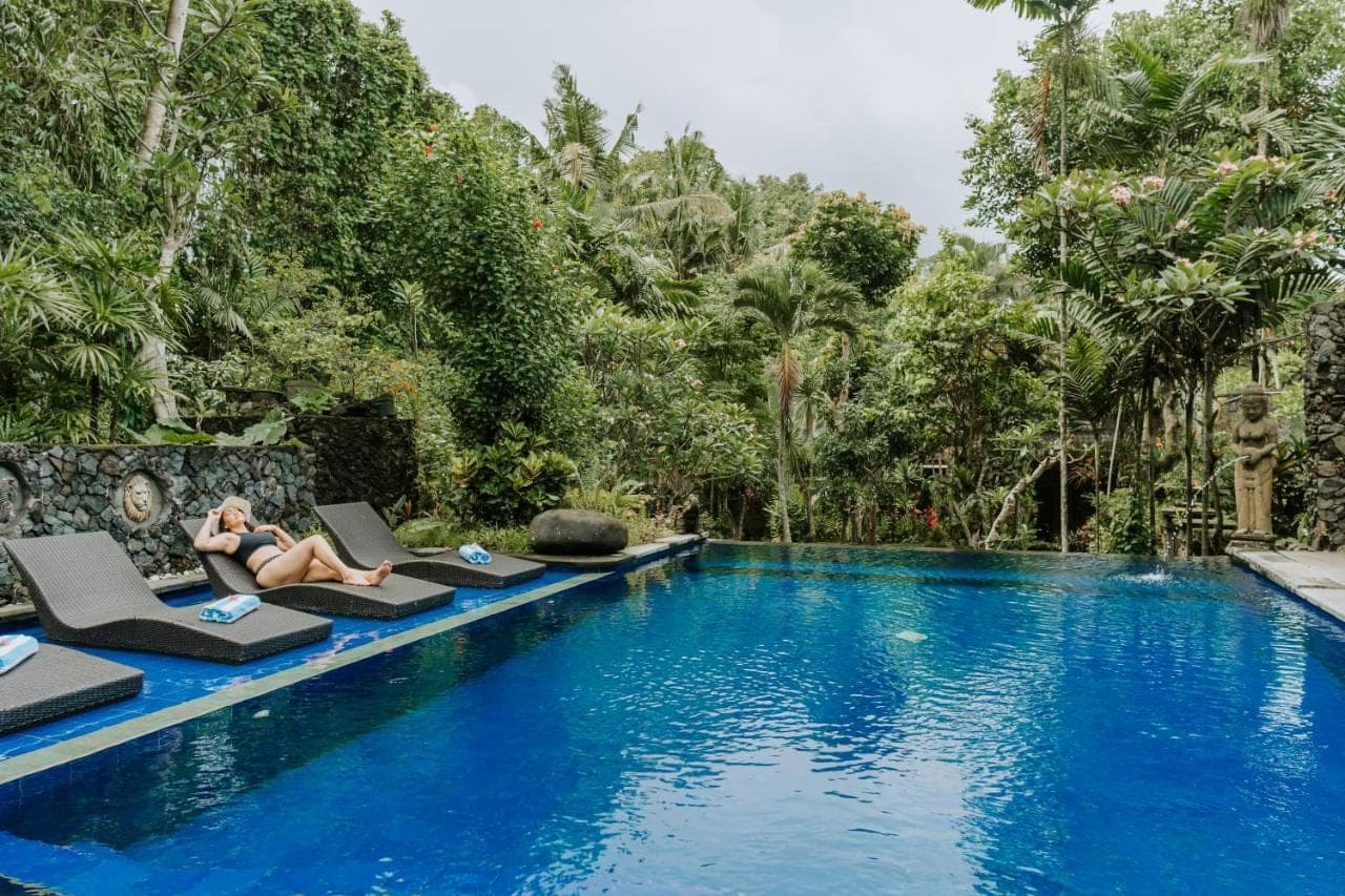 a woman sitting on lounge chairs next to a swimming pool at Dewangga Ubud in Ubud