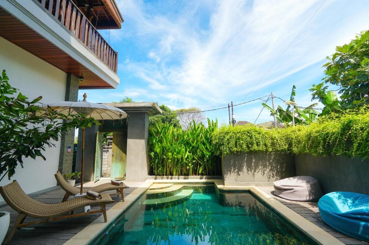 a swimming pool with chairs and an umbrella next to a house at Tropical Beach House Bali in Seminyak