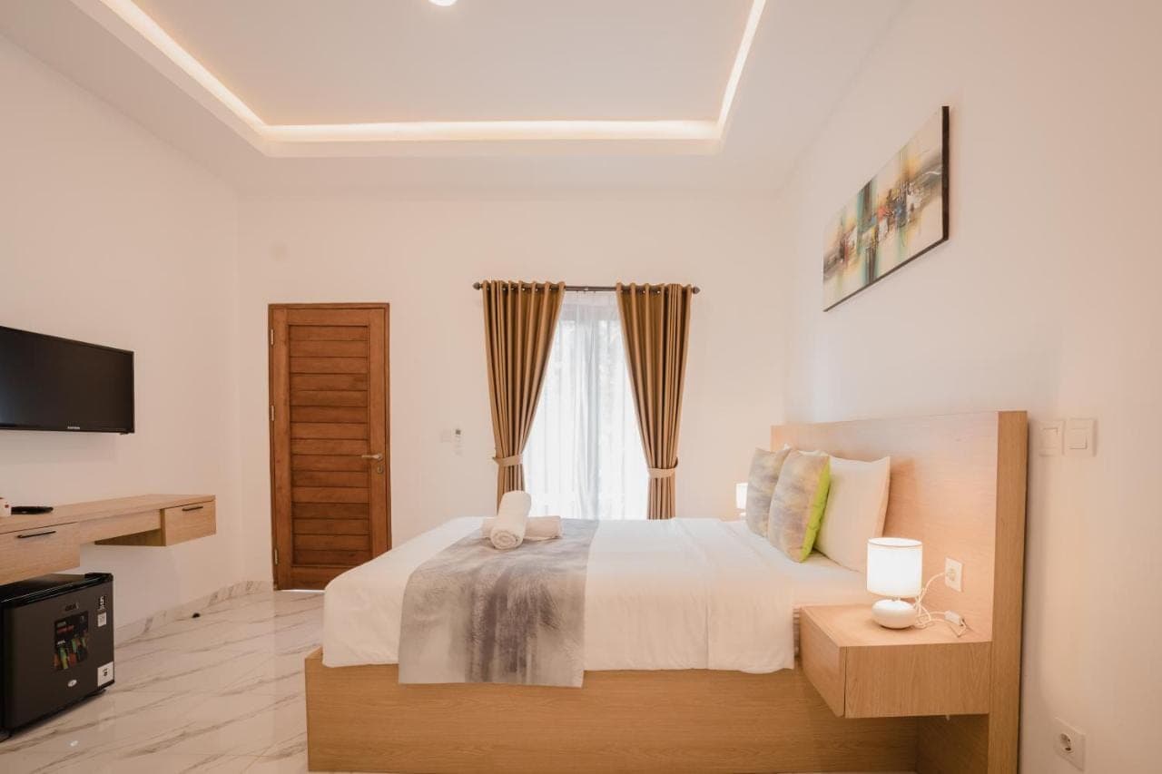 a white bedroom with a bed and a television at Radika Guest House in Uluwatu