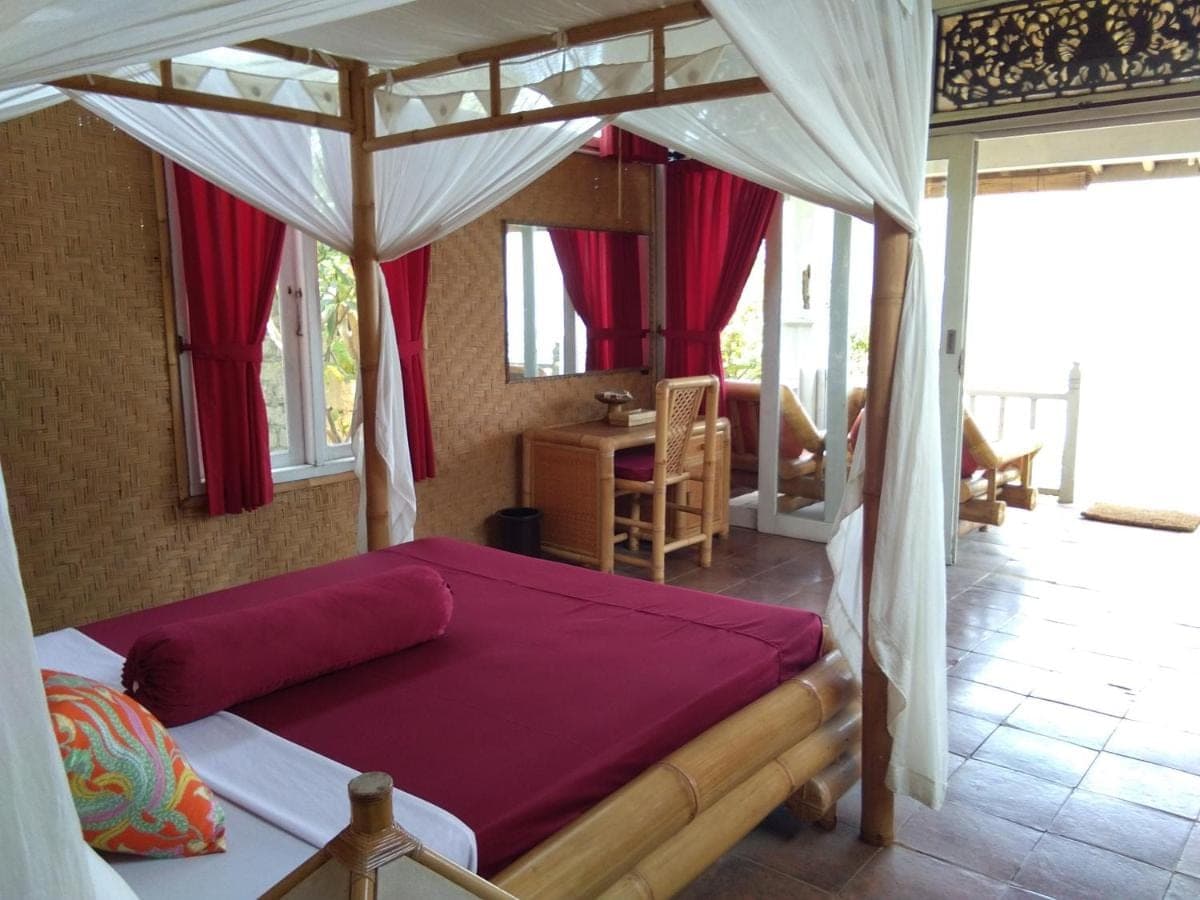 a bedroom with a canopy bed with red sheets at Stairway To Heaven Bungalows and Restaurant in Amed