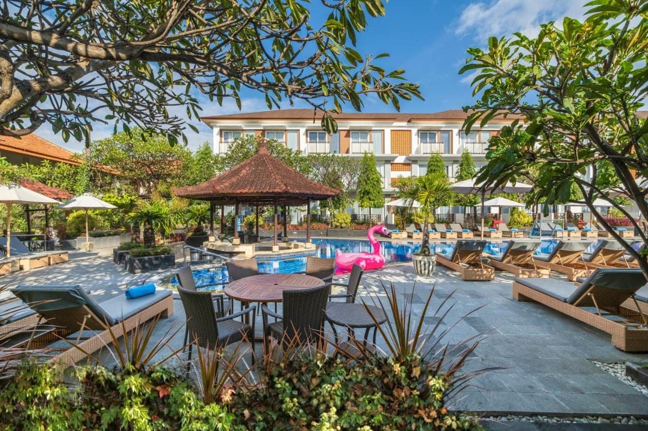 a resort with a pool with chairs and a table at Kuta Beach Club Hotel in Kuta