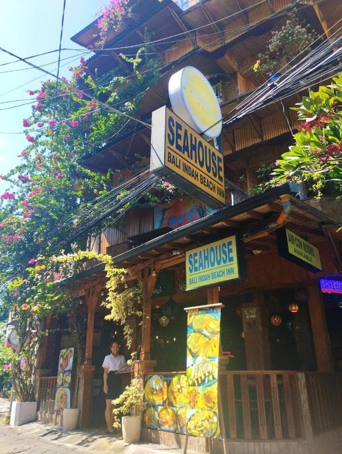 a man standing in front of a restaurant with signs at Seahouse Bali Indah Beach Inn in Kuta