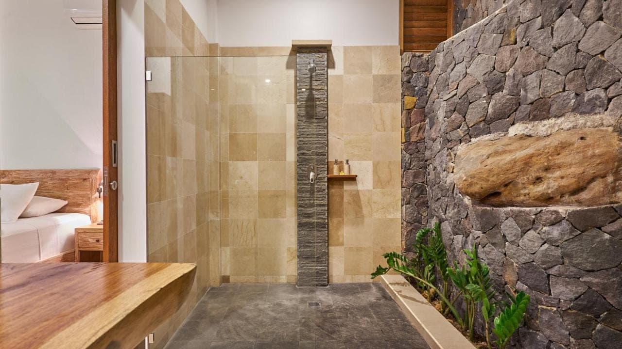 a shower in a bathroom with a stone wall at Villa Aska in Amed