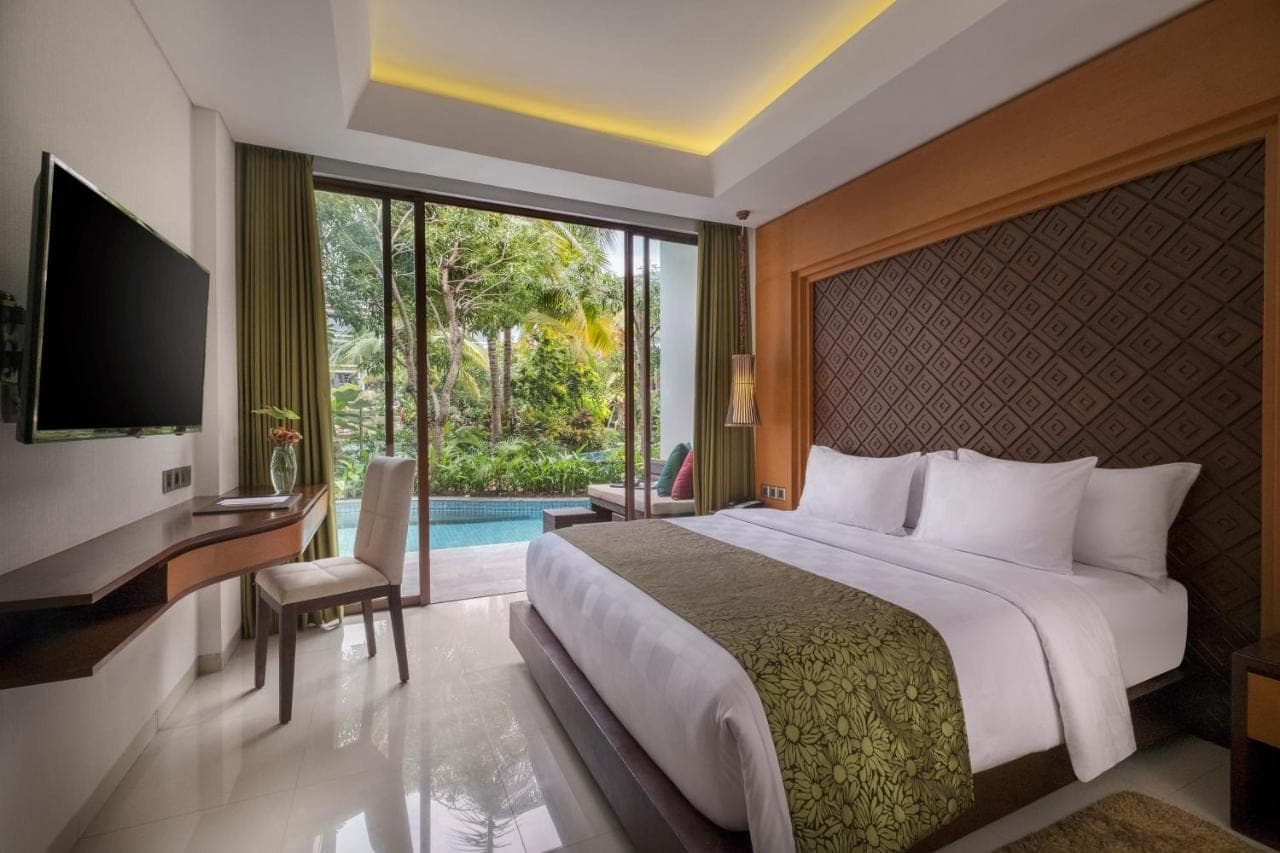 a bedroom with a bed and a tv and a pool at Golden Tulip Jineng Resort Bali in Kuta