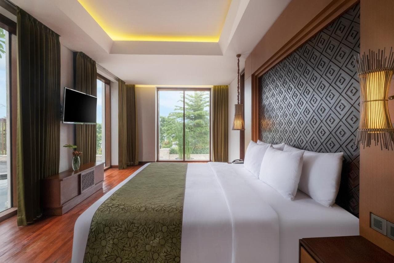 a bedroom with a large bed and a large window at Golden Tulip Jineng Resort Bali in Kuta