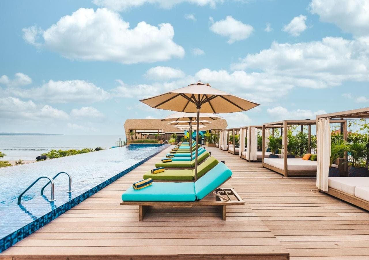a pool with lounge chairs and an umbrella and the ocean at MAMAKA Bali in Kuta