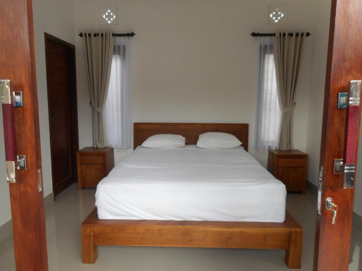 a bedroom with a white bed and two windows at New Lilastana Homestay in Sidemen