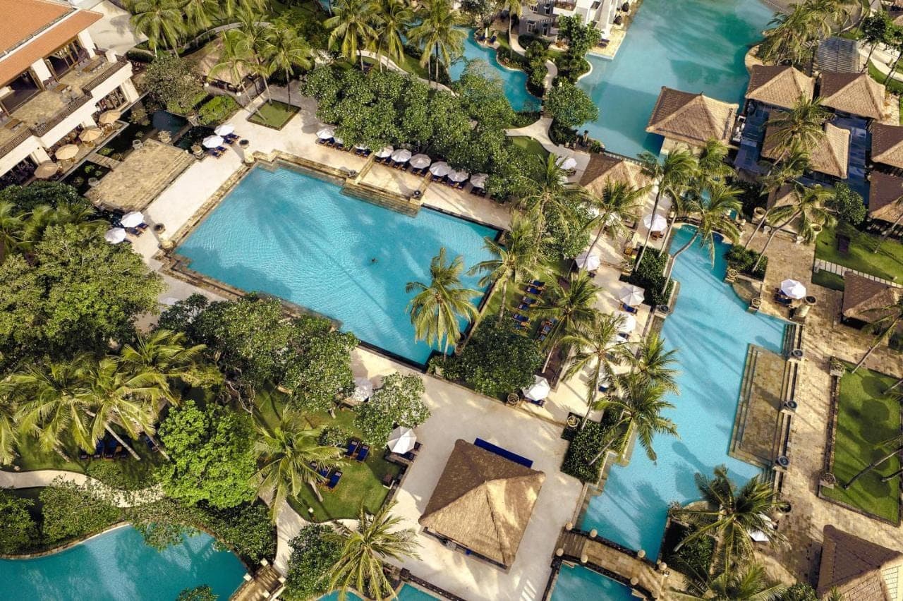 an aerial view of a resort pool with palm trees at Conrad Bali in Nusa Dua