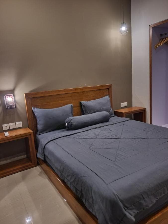 a bedroom with a bed with blue sheets and two tables at Kalih Homestay Bali in Kuta