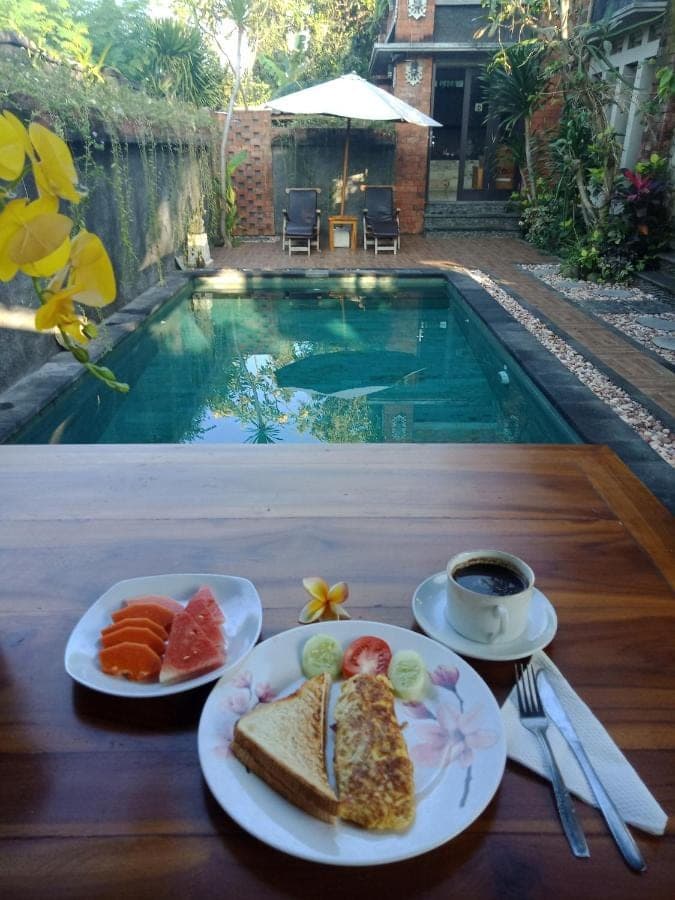 a table with plates of food next to a swimming pool at D'puja Home Stay and Spa in Nusa Dua
