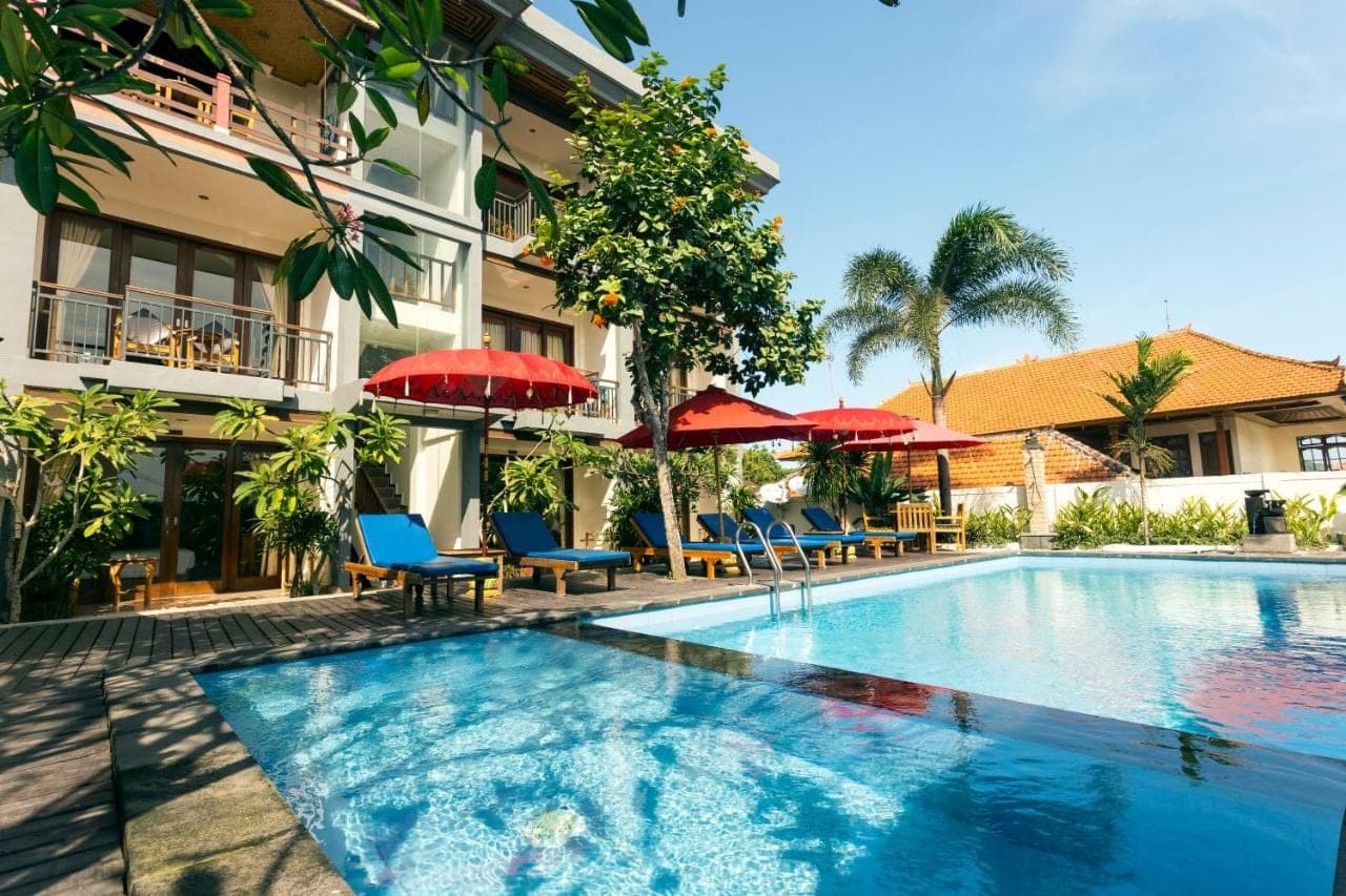 a swimming pool with chairs and umbrellas next to a building at Waroeng Surya Home Stay in Uluwatu