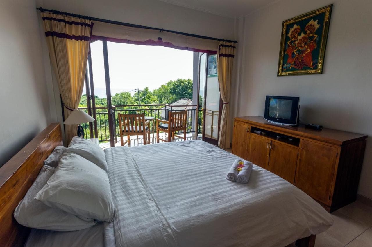 a bedroom with a bed and a balcony with a television at Waroeng Surya Home Stay in Uluwatu