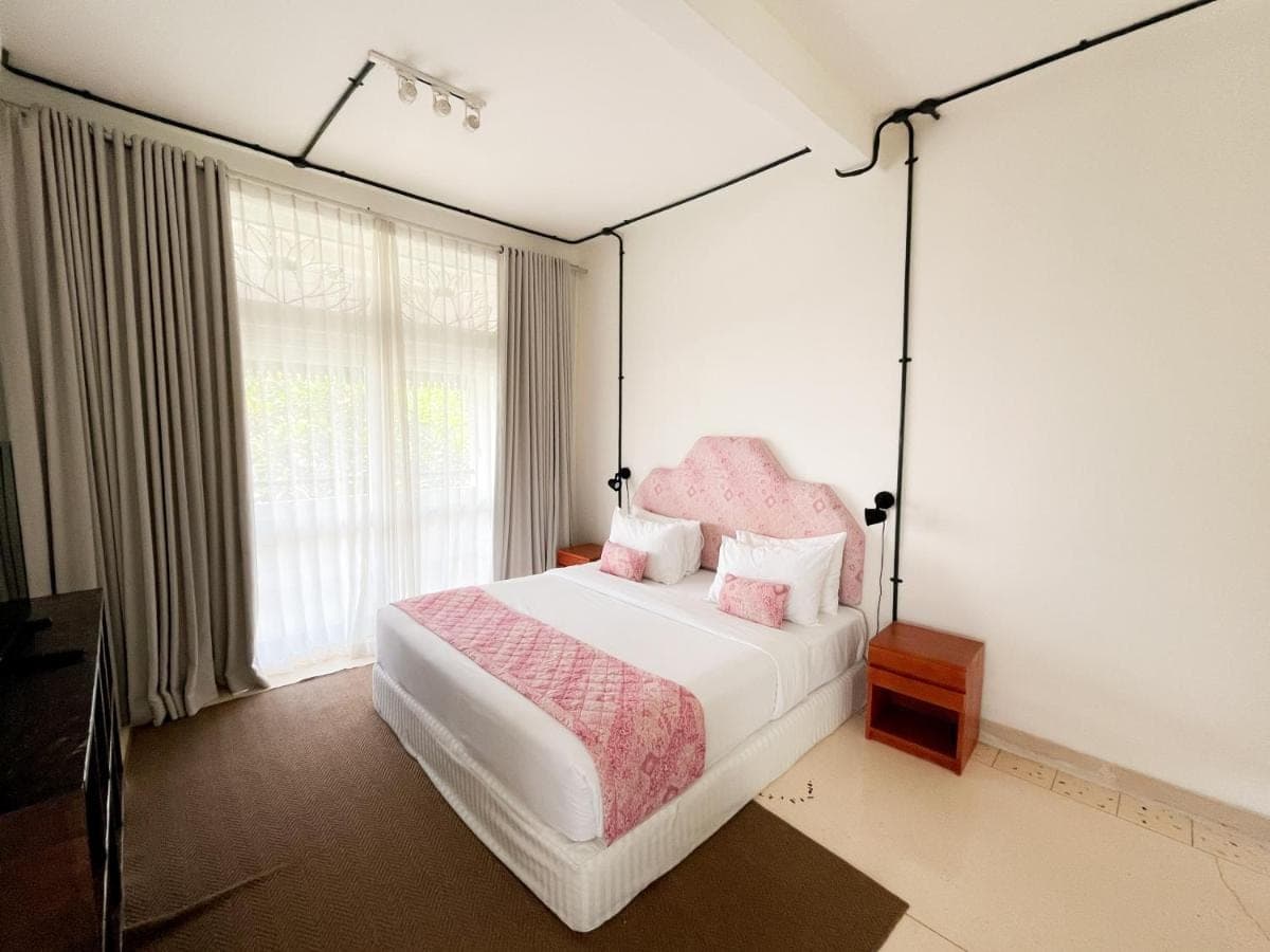 a bedroom with a large bed with a pink headboard at Kresna By The Sea By Kresna Hospitality in Seminyak