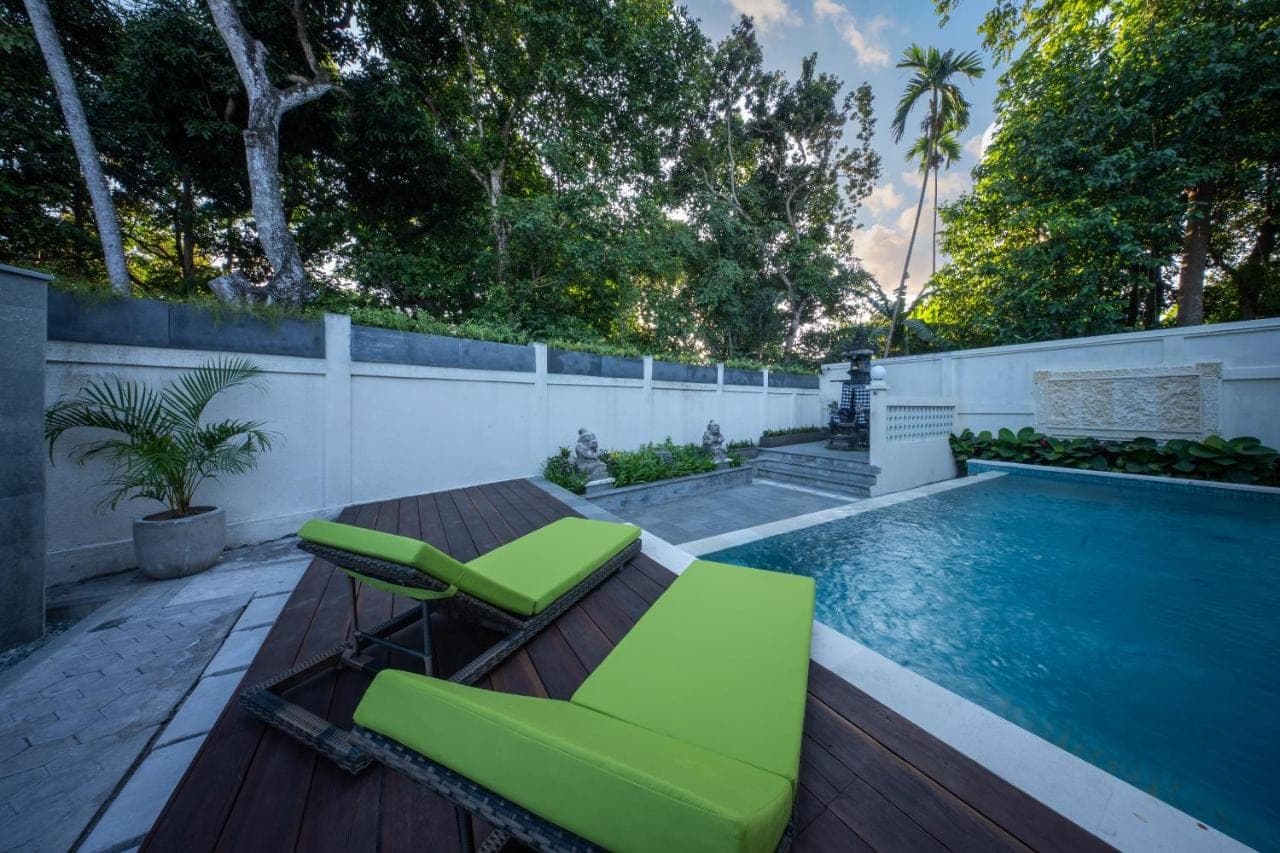 a swimming pool with two green chairs next to a wooden deck at Sadira Guest House Seminyak in Seminyak