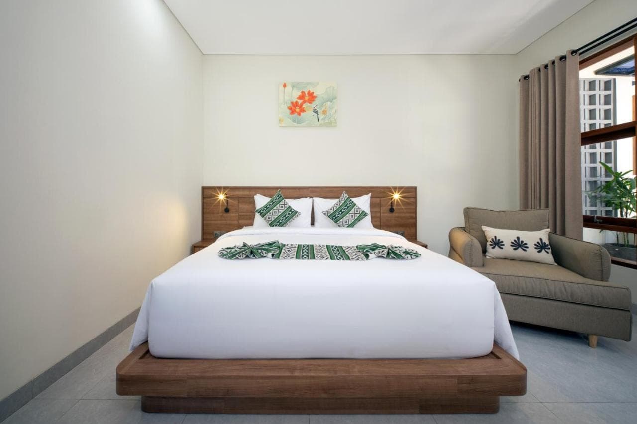a bedroom with a large white bed and a chair at Sadira Guest House Seminyak in Seminyak