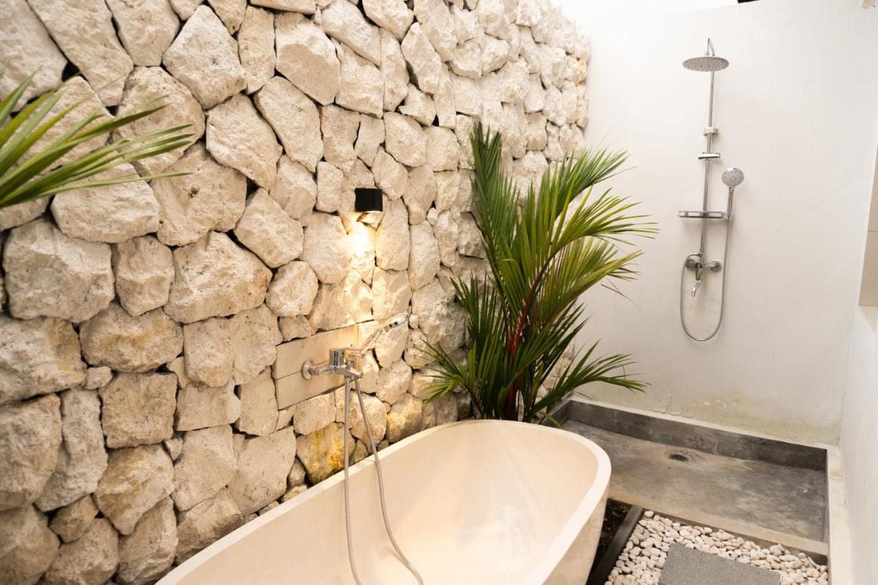 a bathroom with a stone wall and a bath tub at The Ume Sidemen Villas in Sidemen
