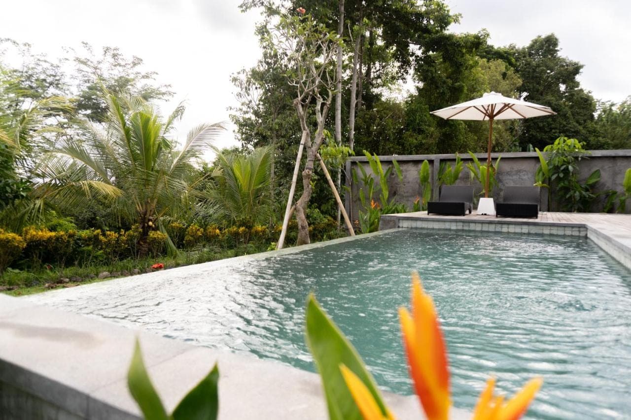 a swimming pool with two chairs and an umbrella at The Ume Sidemen Villas in Sidemen