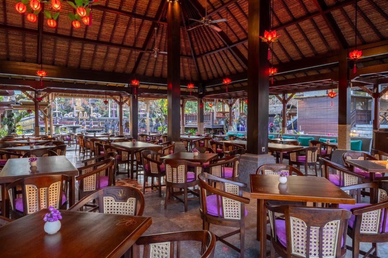 an empty restaurant with wooden tables and chairs at Puri Saraswati Dijiwa Ubud in Ubud