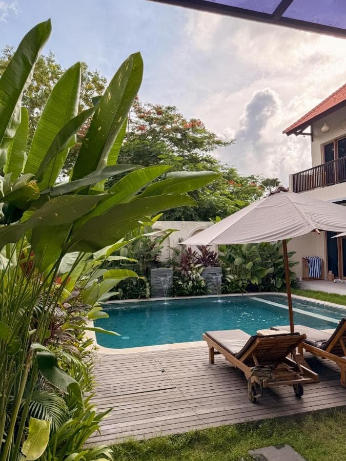 a swimming pool with an umbrella and a chaise lounge next to a house at Wanaseta Guesthouse in Uluwatu