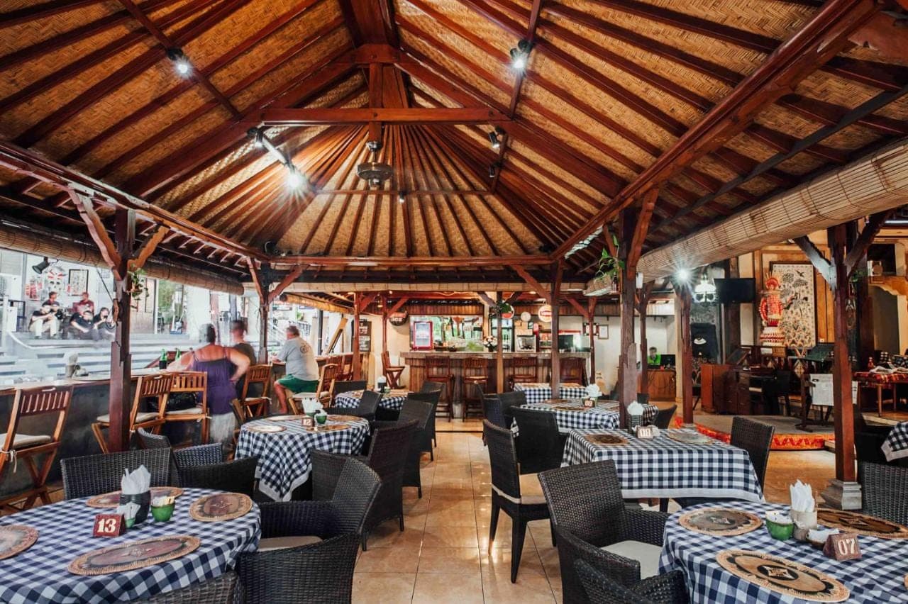 a restaurant with tables and chairs and a wooden ceiling at Kuta Puri Bungalows, Villas and Resort in Kuta