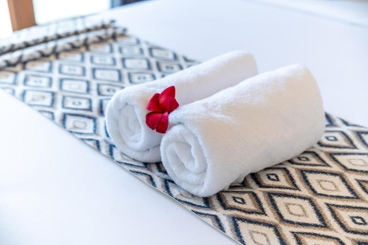 a white towel with a red flower on a bed at Erira House Ubud in Ubud