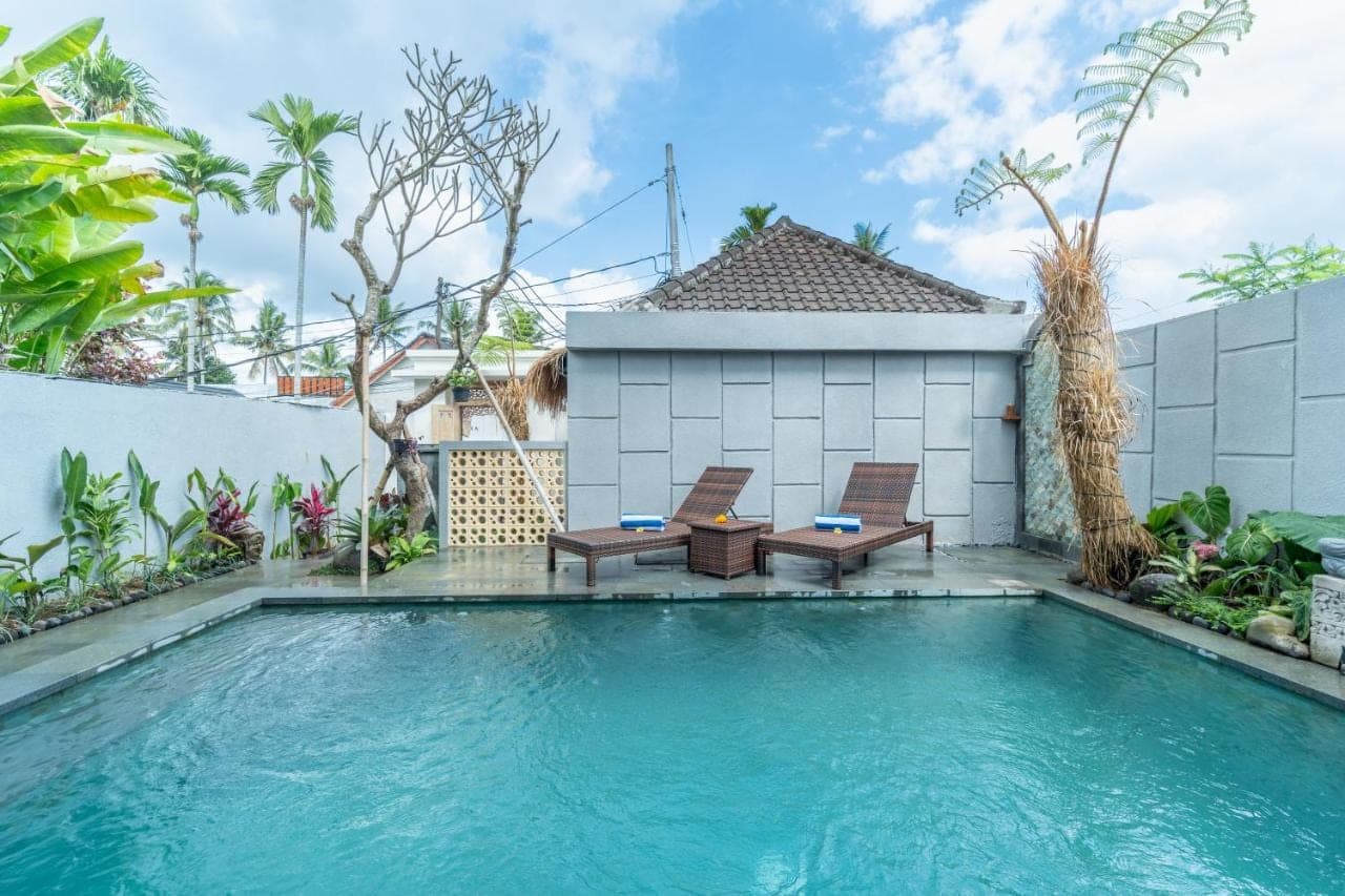 a swimming pool with two chairs and a house at Erira House Ubud in Ubud