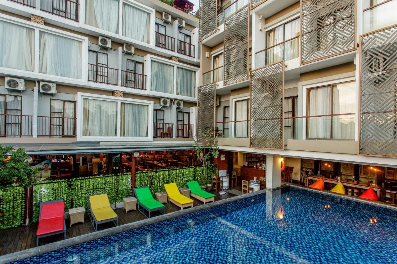 an apartment building with a swimming pool and colorful chairs at Metland Seva Seminyak - Formerly Horison Ultima Seminyak in Seminyak