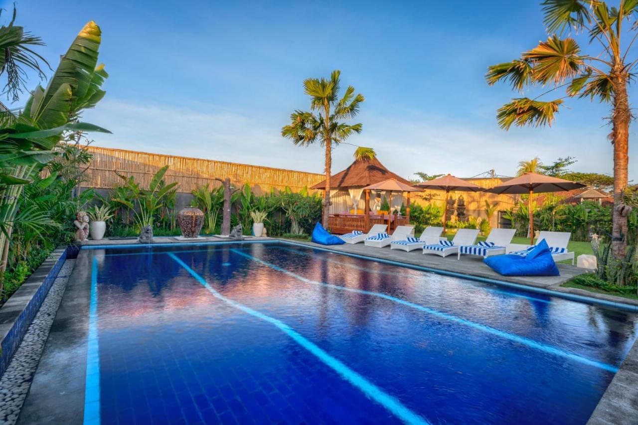 a swimming pool with chairs and palm trees at Kubu Dimel Suites and Villas Resort in Nusa Dua