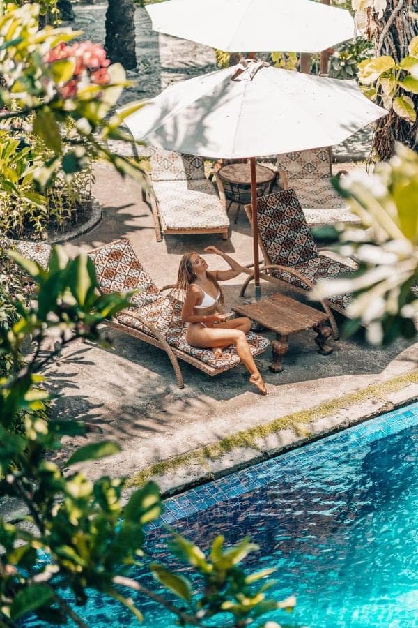 a woman sitting on a chair next to a swimming pool at Hotel Tugu Bali, Canggu in Canggu