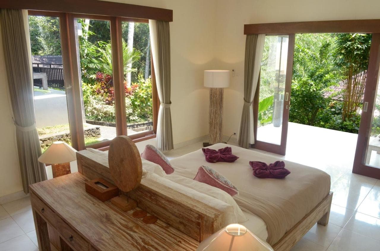 a bedroom with a large bed and large windows at The Bali Shanti in Ubud