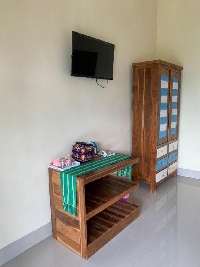 a room with a table and a tv on a wall at Makna Homestay and Spa in Sidemen