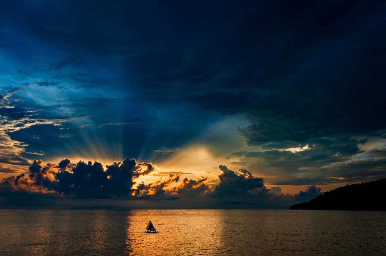 a boat in the water under a cloudy sky at Aquamarine Seaview Villa in Amed
