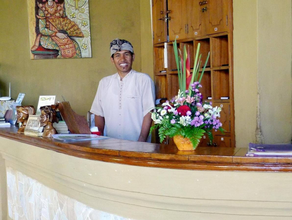 a man standing behind a counter with flowers at Santai Hotel in Amed