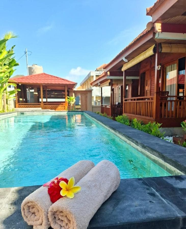 a resort swimming pool with towels and a flower on the edge at Pondok Denly by Pigeon in Nusa Dua