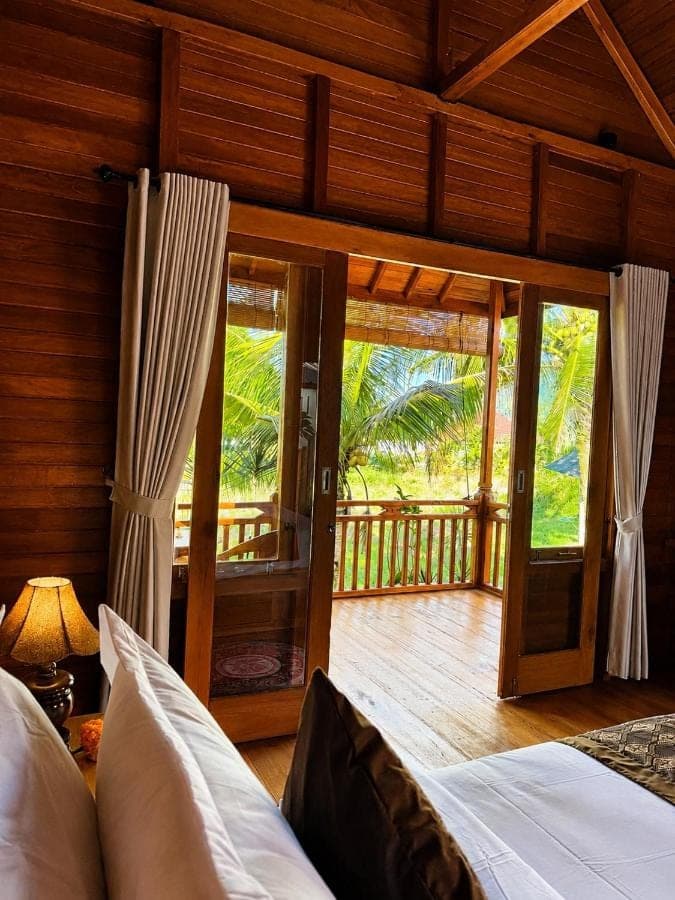 a bedroom with a bed and a balcony with sliding glass doors at Deva Graha Sidemen in Sidemen