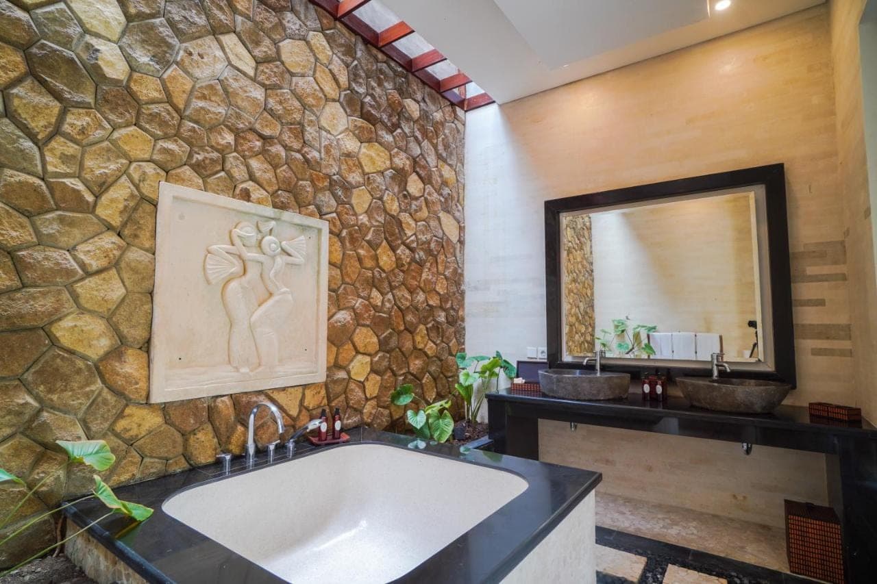 a bathroom with a large tub and a stone wall at Giri Bhagawan Villas & Spa in Nusa Dua